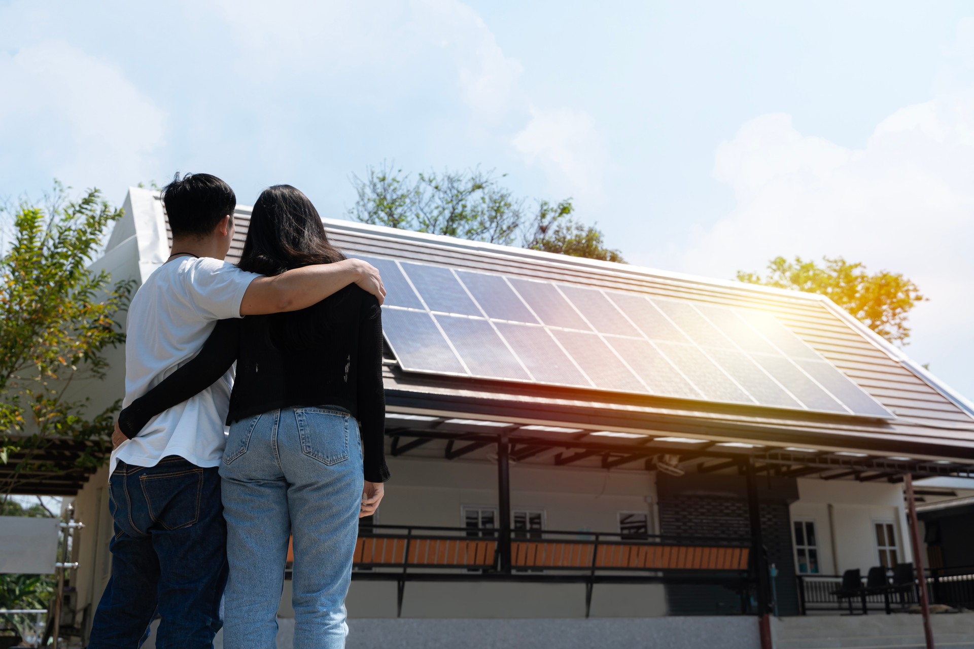 Happy couple standying near their house with solar panels. Alternative energy, saving resources and sustainable lifestyle concept.